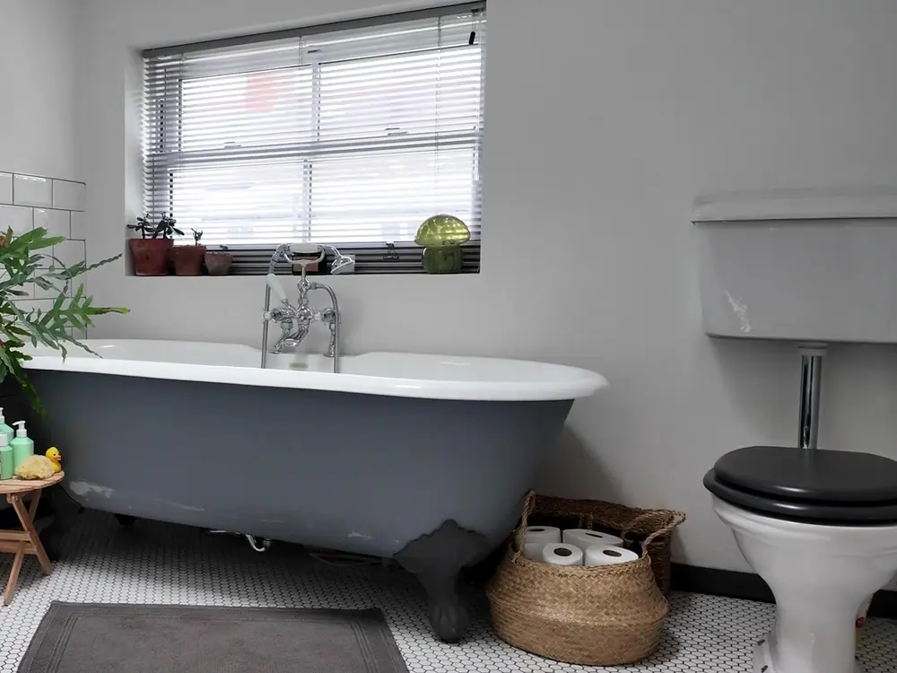 A bathroom with a grey roll-top bath, white tiles and a high-level cistern