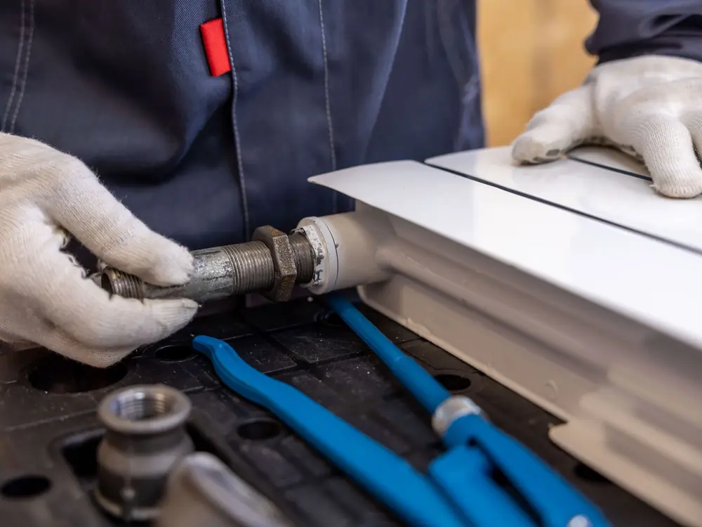 Gloved hands tightening a valve onto the end of a radiator
