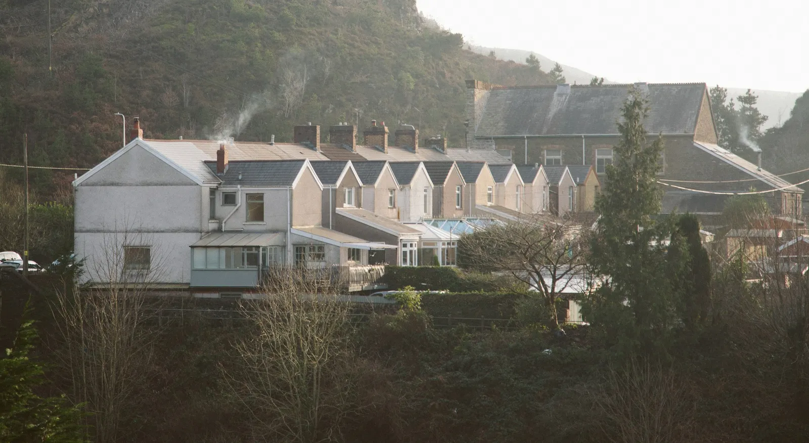 A row of terraced houses with slate roofs and chimneys below a hillside