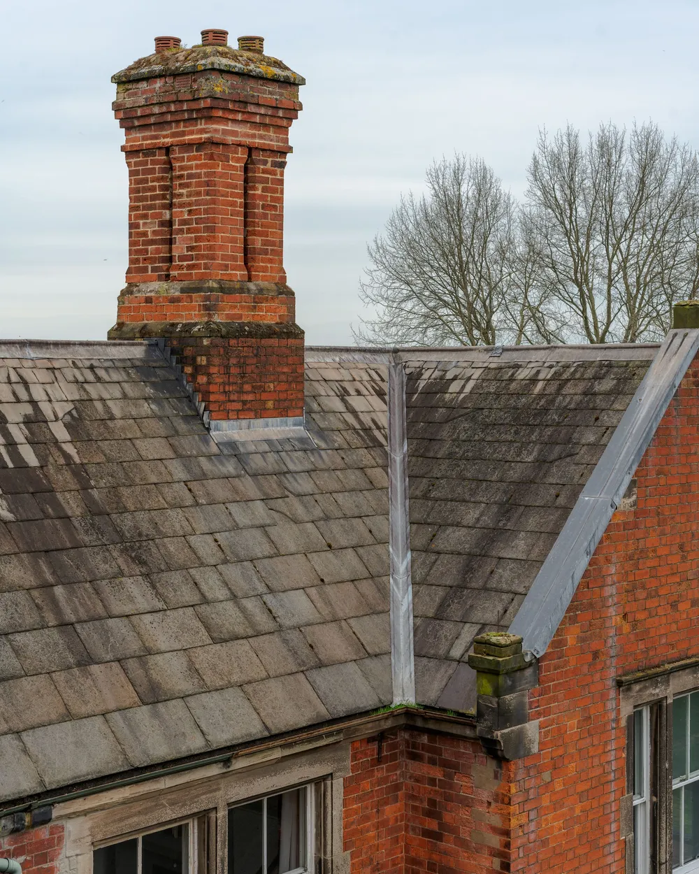 A brick chimney on an old slate roof, with lead flashing at its base and a lead-lined valley where two slopes meet