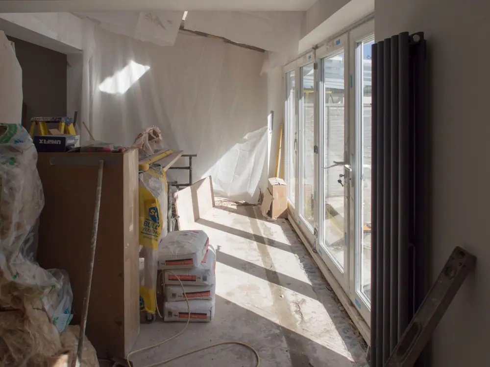 Inside a new rear extension before decorating, with glazed doors along one side and building materials stacked by the wall
