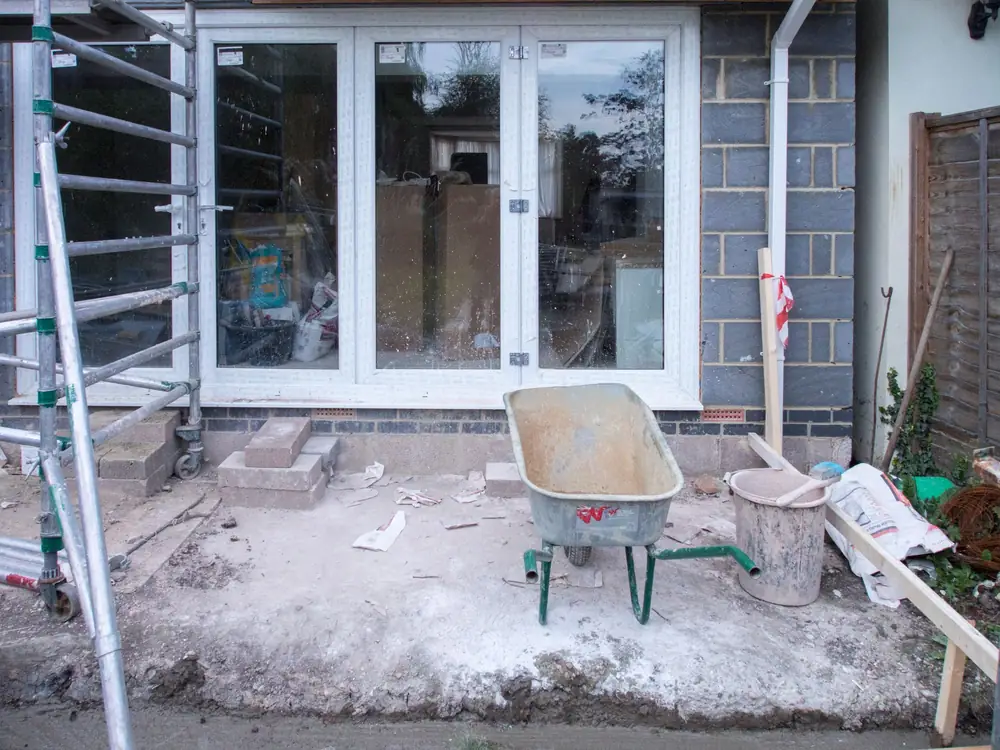 New glazed doors set into a blockwork wall, with a wheelbarrow and scaffold tower on the bare ground outside