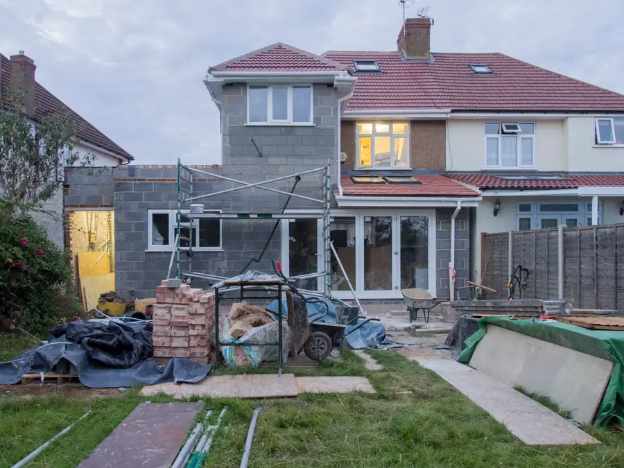 A rear extension part built in grey blockwork, seen from the garden, with materials under tarpaulins on the lawn