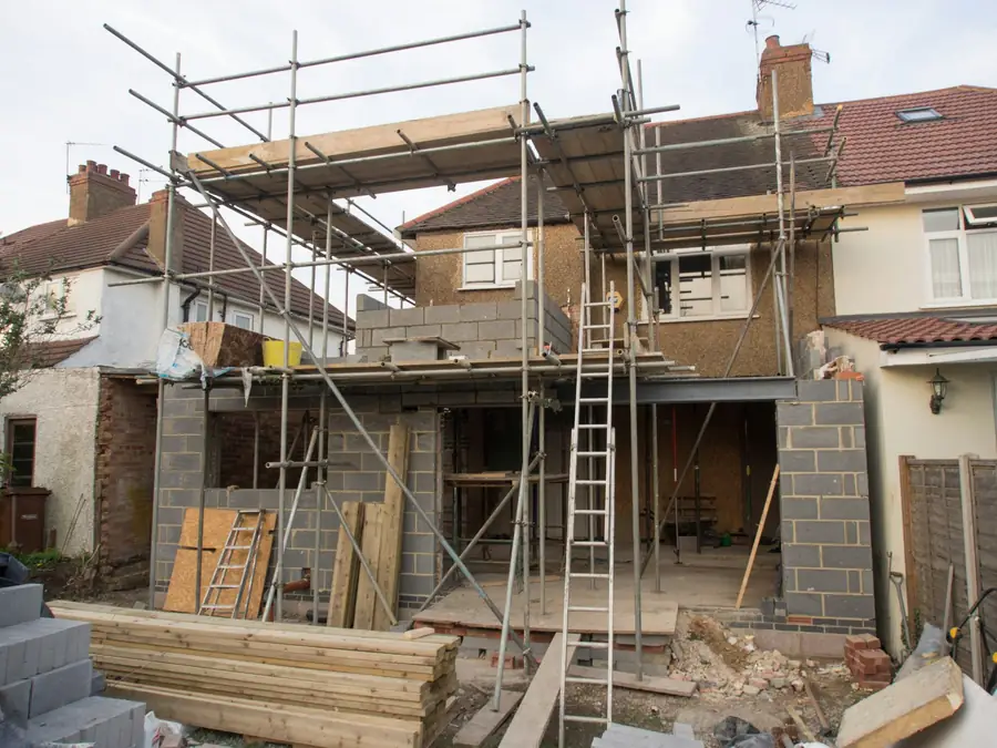 Scaffolding around an extension going up at the back of a semi-detached house, with timber stacked in front